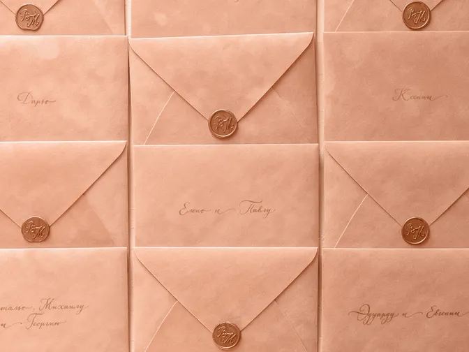 Rows of peach wedding invitation envelopes sealed with wax, each addressed by hand in calligraphy.