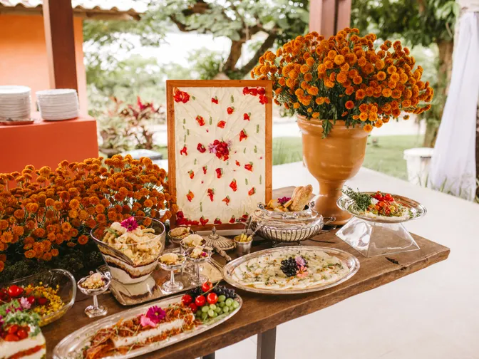 A generous outdoor wedding buffet table crowded with dishes and bright orange marigold arrangements.
